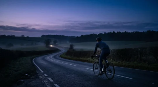 Cyclist riding on a dark country lane at dusk with subtle reflective elements catching vehicle headlights