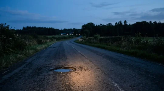 Close-up of bicycle front light illuminating dark asphalt road surface with textured details visible