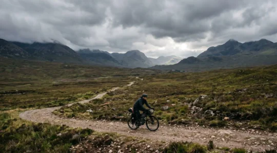 Lone bikepacker navigating rugged Highland terrain under dramatic Scottish sky
