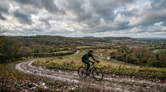 Gravel bike rider navigating muddy British countryside trail with chalk hills in background